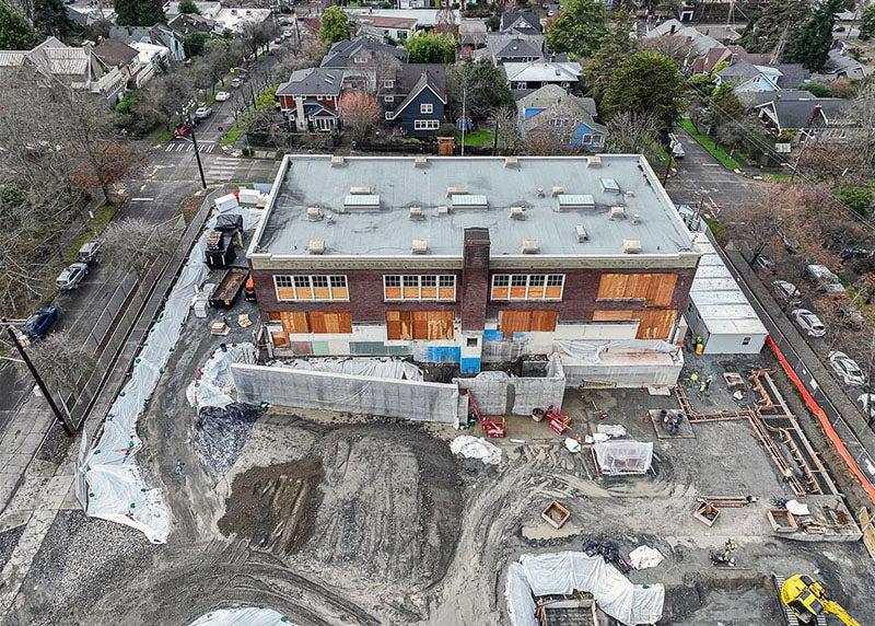 at brick building with boarded up windows sits in a construction site with a concrete wall in front