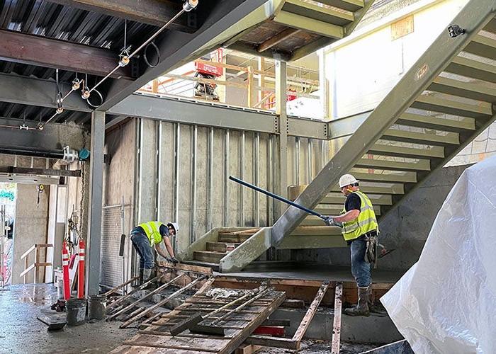 interior of a partially built wall and ceiling with a stairway being built by 2 workers