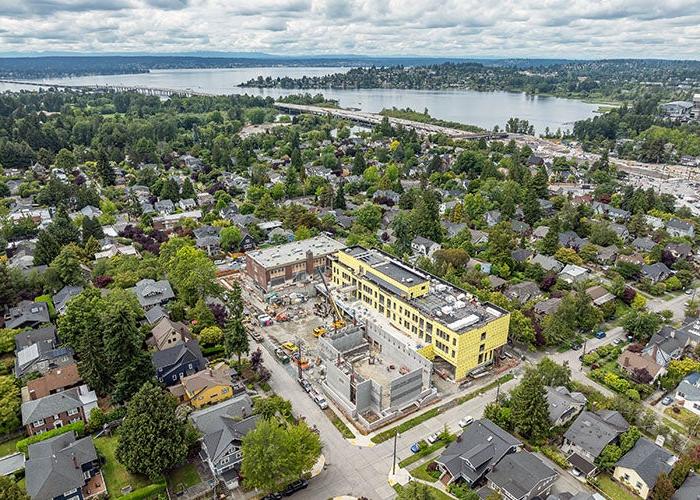 aerial view of entire construction site showing historic brick building, new addition, gym construction in progress, and the surrounding neighborhood with the lake in the background