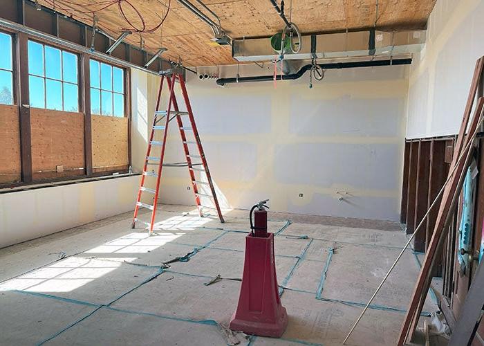 a room under construction with windows on one side and built in cupboards on the other. ductwork and conduit is on the ceiling