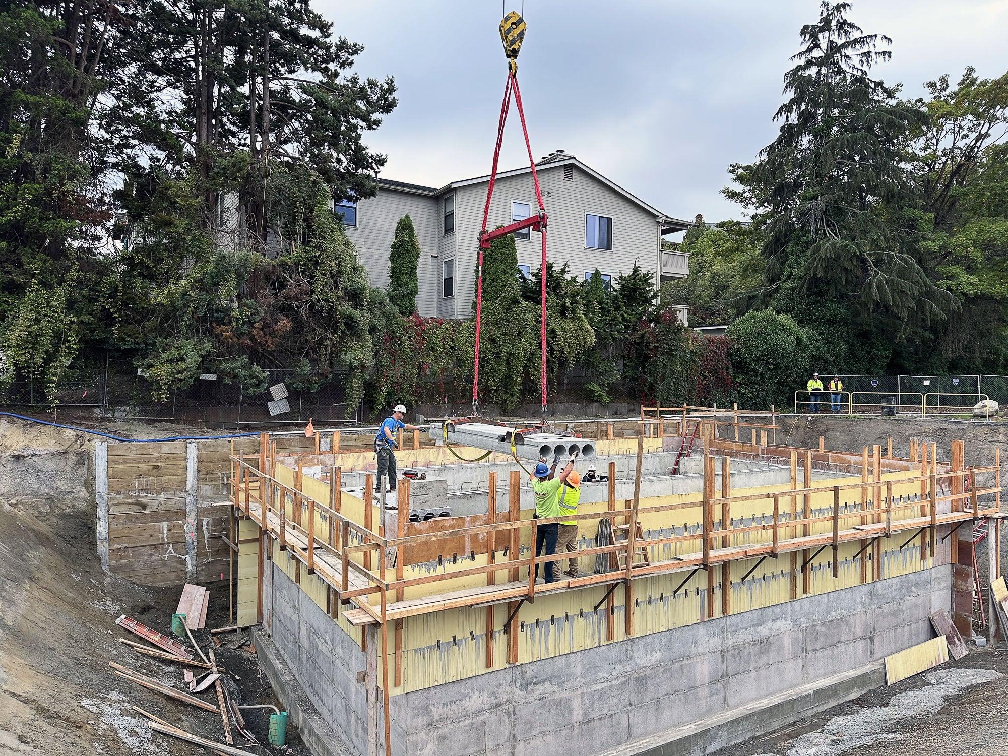 people working to lower material on top of concrete box using a crane