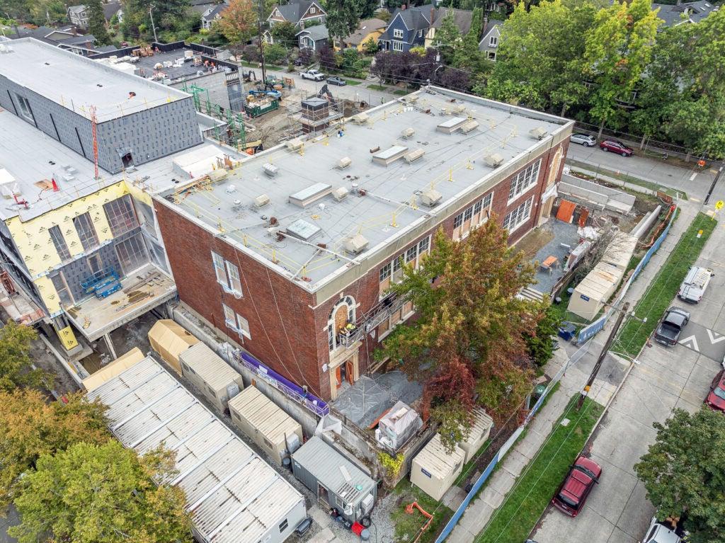 brick building with trees in front and a building under construction attached