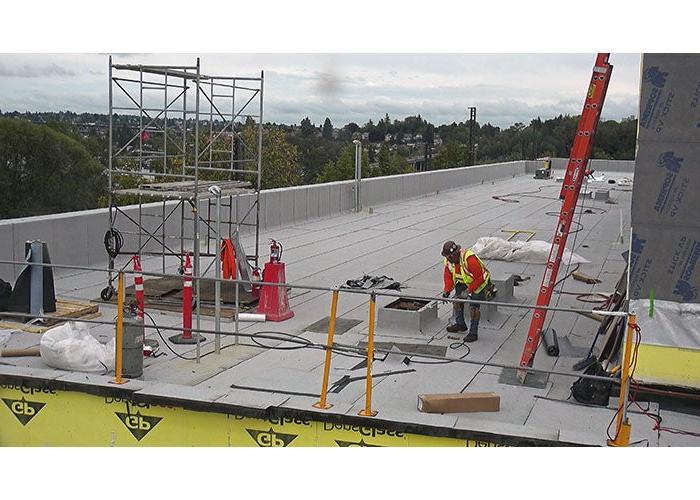 part of a flat roof with a ladder and scaffold and a worker in a vest and hardhat