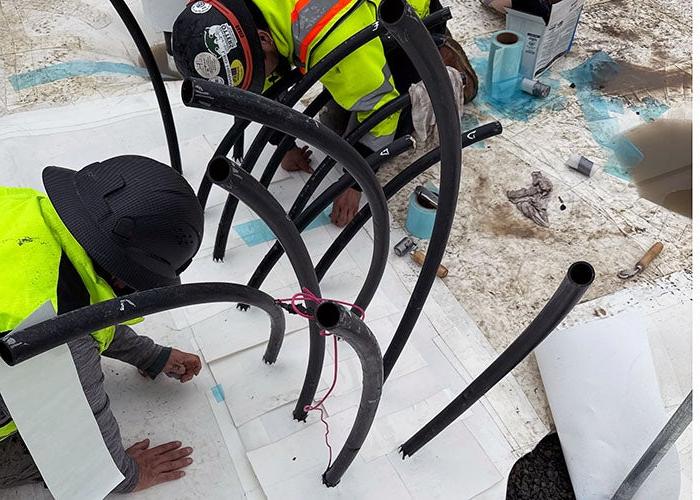 rubber piping sticking up with white material being installed around each pipe by workers